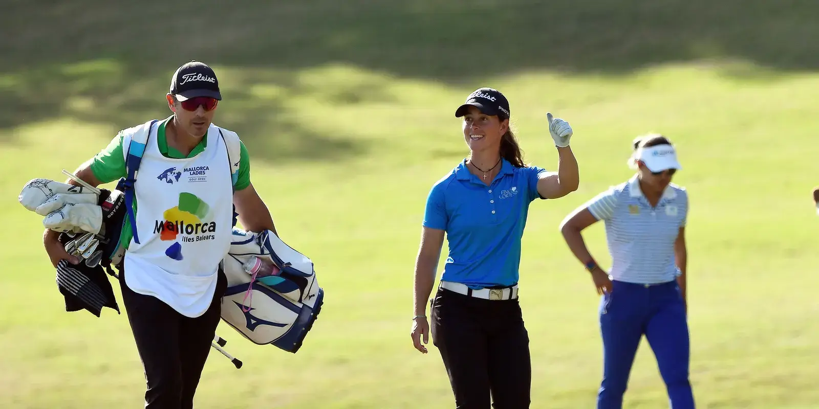 Leende golfspelare ger tummen upp på fairway, med caddie och medspelare i solsken