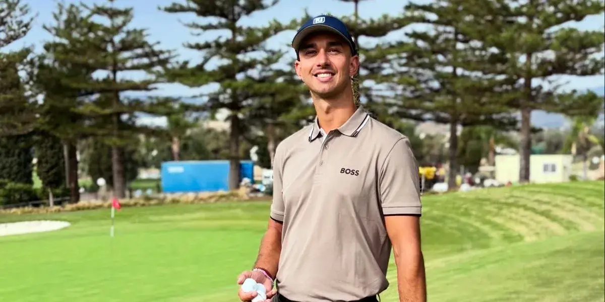 Magnus Brovold smiler med golfbolde og putter i hånden på en golfbane med høje træer i baggrunden